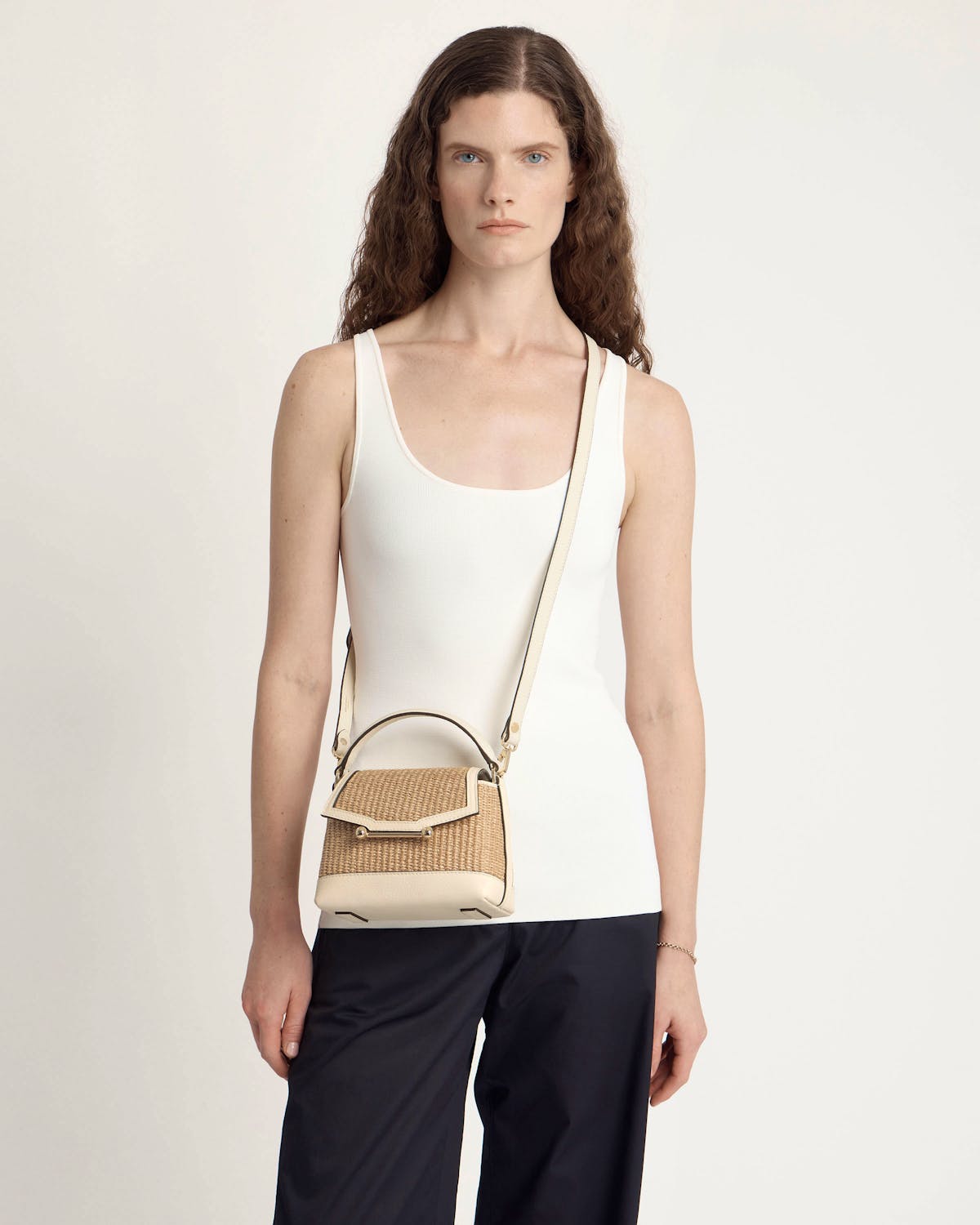Model wearing a small vanilla and natural raffia cross-body bag with leather trim