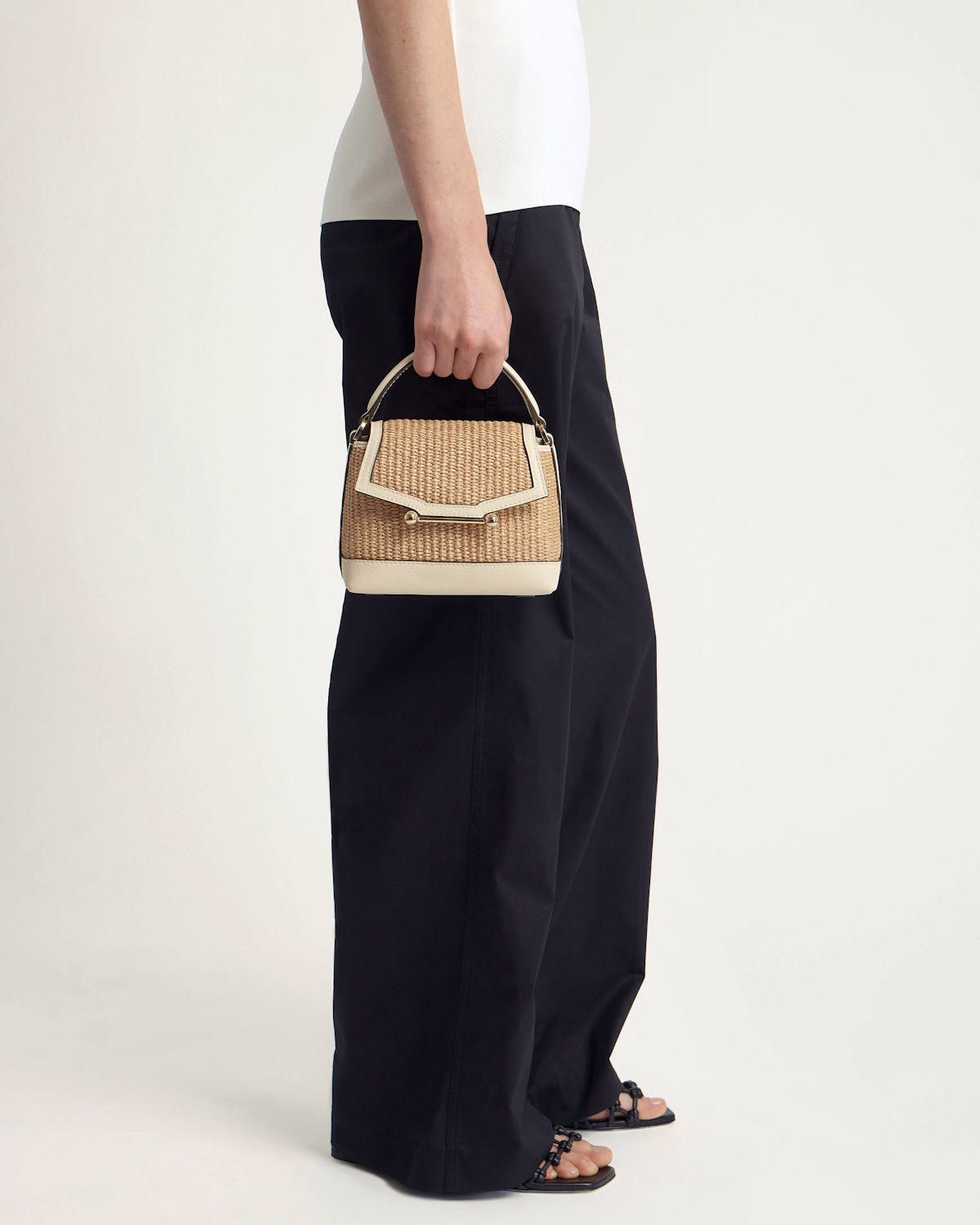 Model holding small woven raffia top-handle bag with vanilla leather trim.