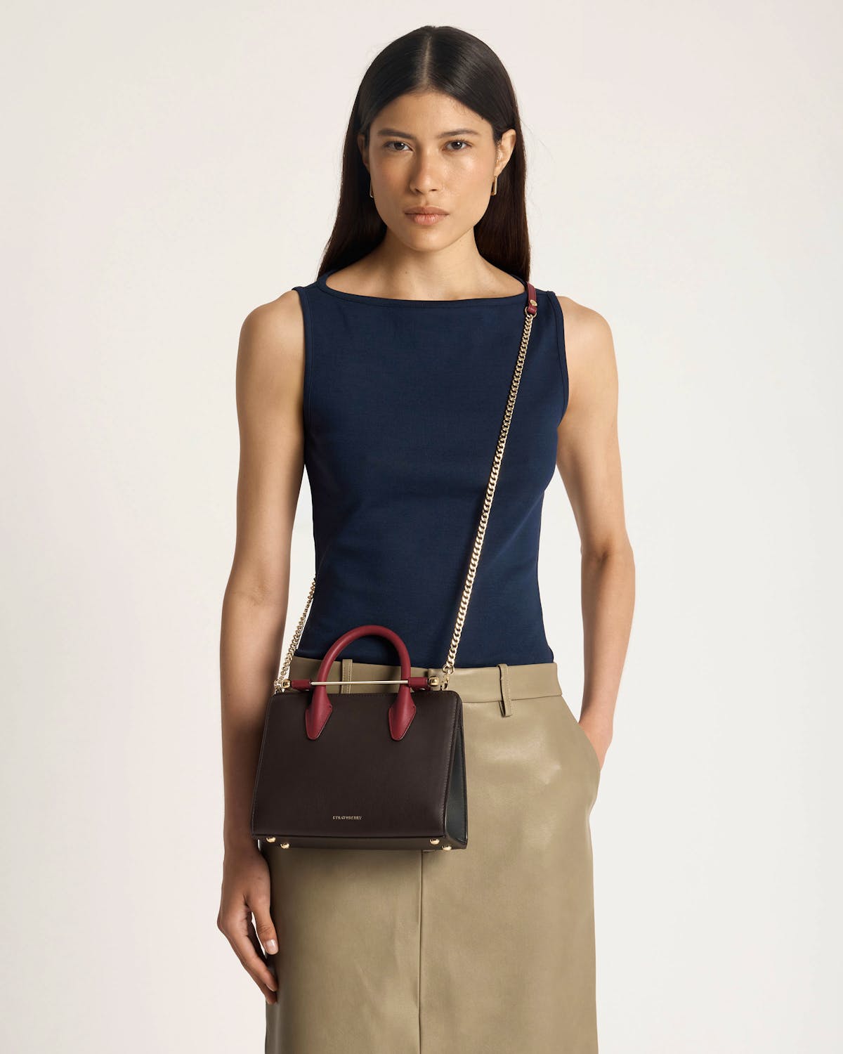 Model wearing a Strathberry mini tote in espresso with oxblood handles and gold chain strap