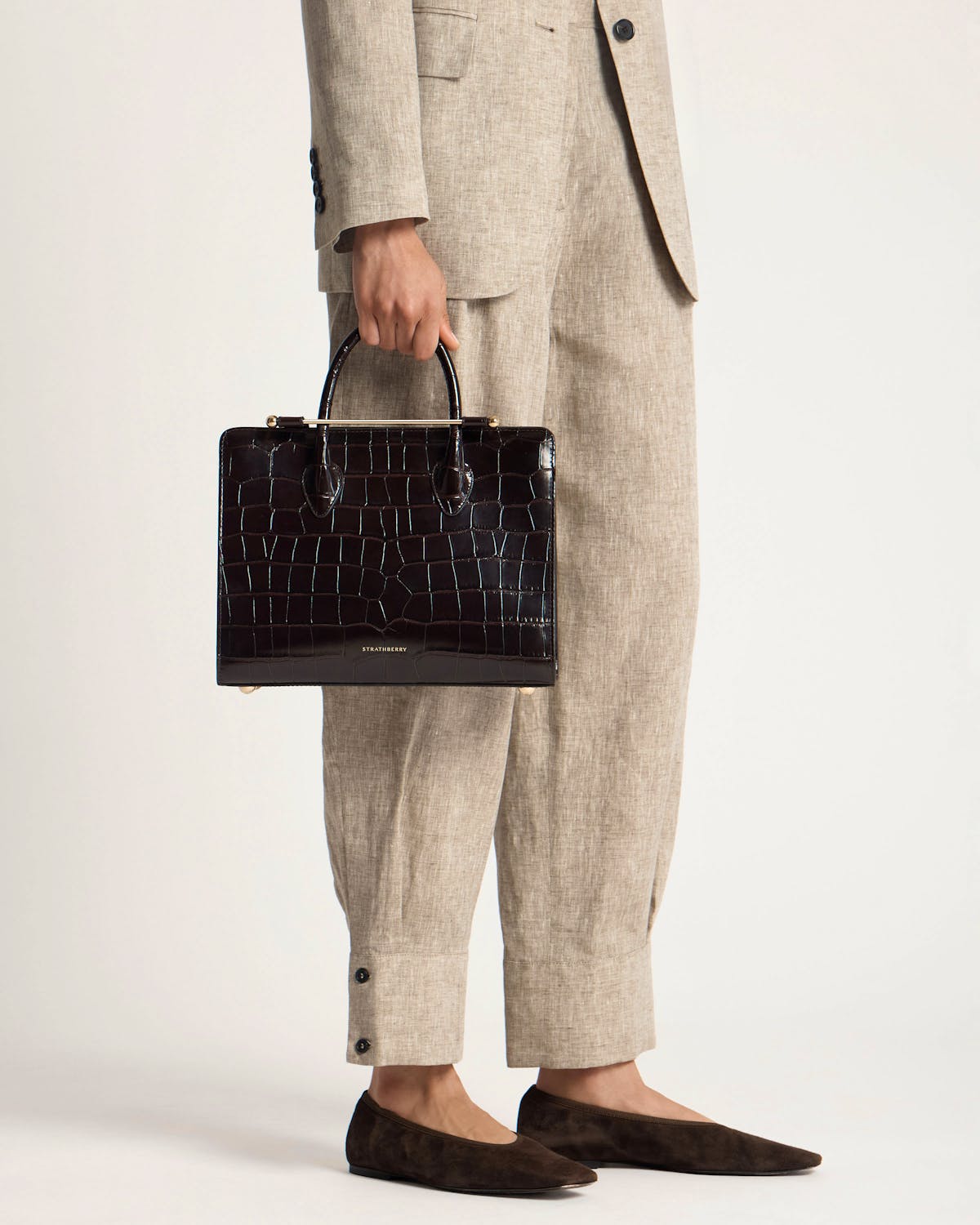 Strathberry croc midi tote held by model wearing beige suit trousers.