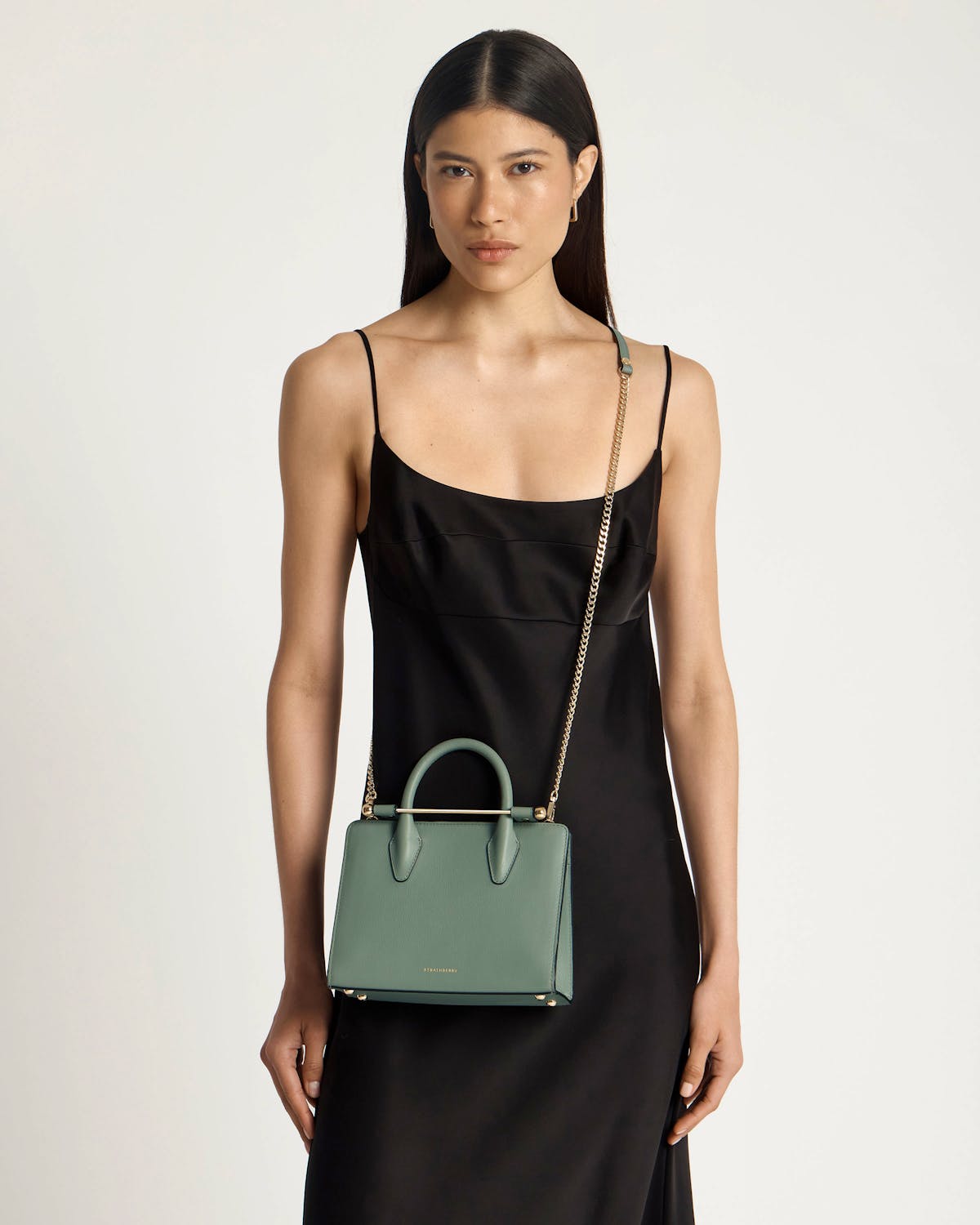 Model wearing black slip dress with Strathberry library green mini tote, gold chain strap.