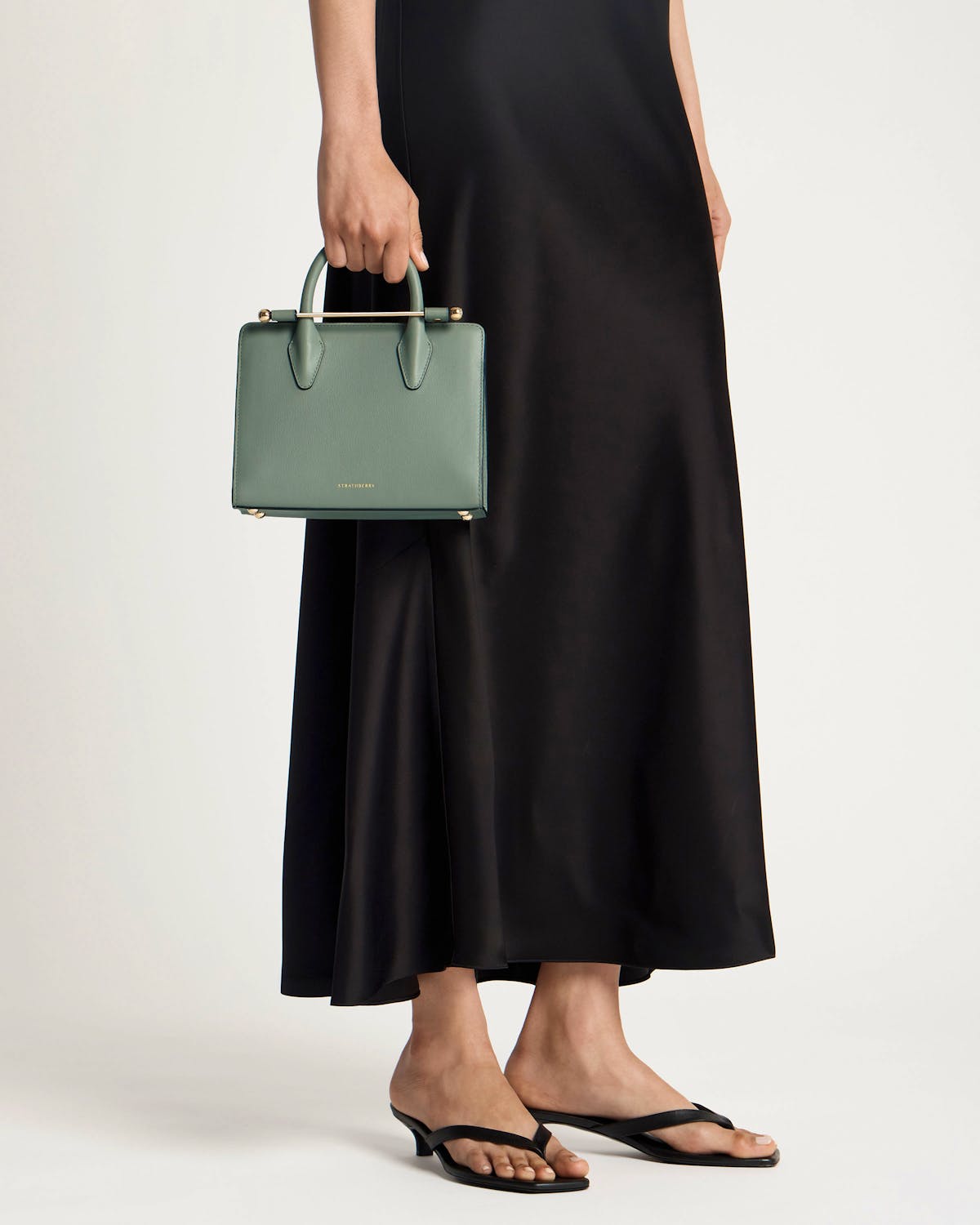 Library green Strathberry mini tote held by model, gold bar handle visible.