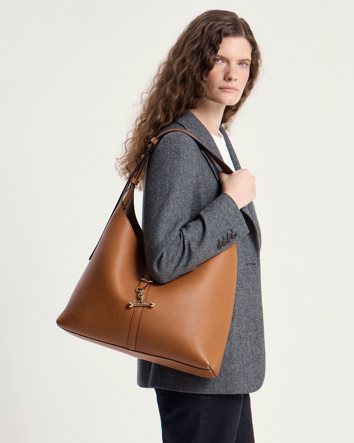 Woman wearing a tan leather hobo bag on her shoulder, grey blazer.