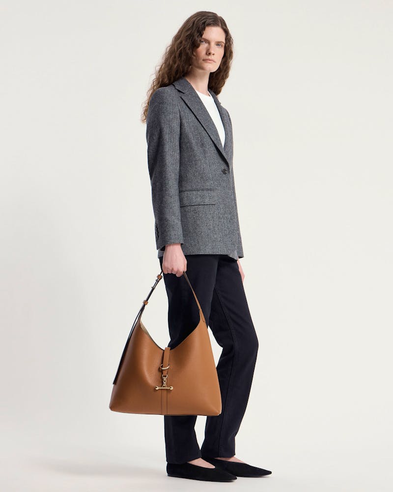 Model wearing grey blazer and black trousers holding tan Kite Hobo Maxi bag.