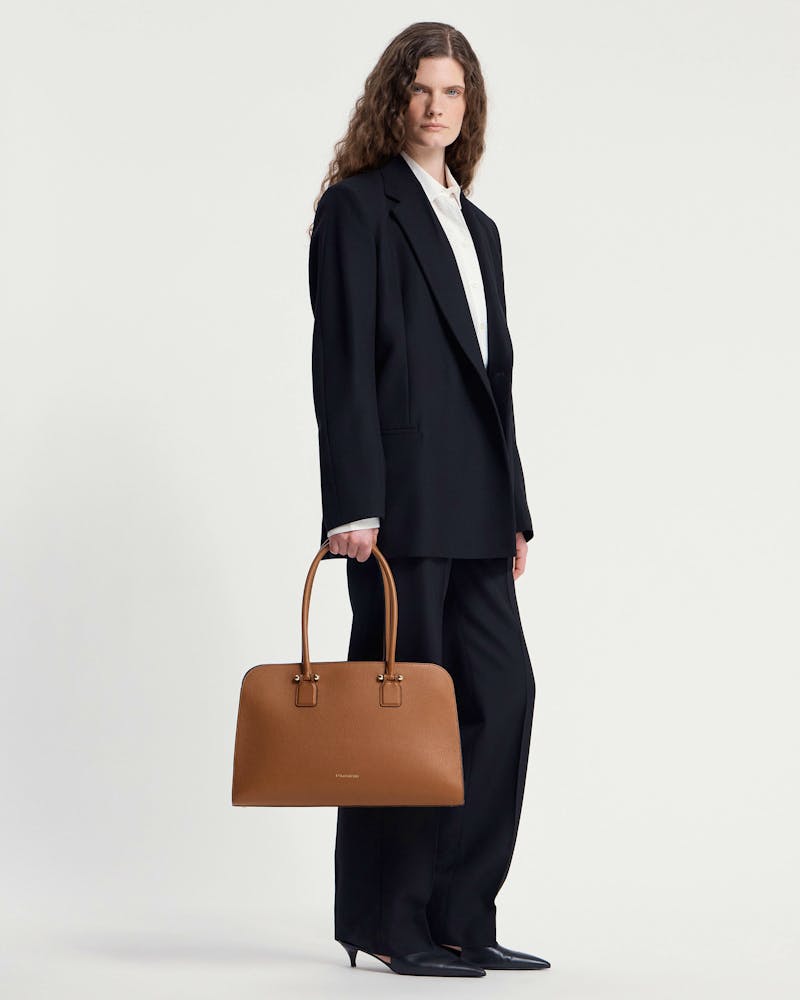 Model holding tan Georgia Maxi tote bag with Strathberry logo and double handles.