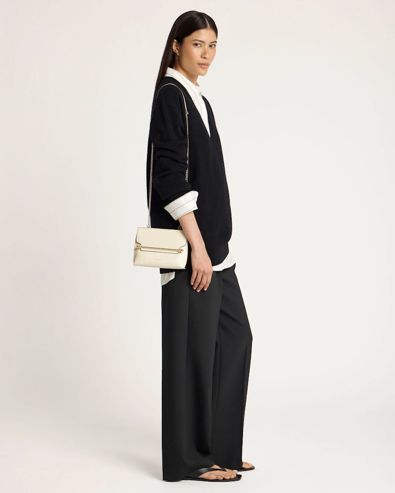 Model wearing black outfit holds a vanilla mini shoulder bag with chain strap.
