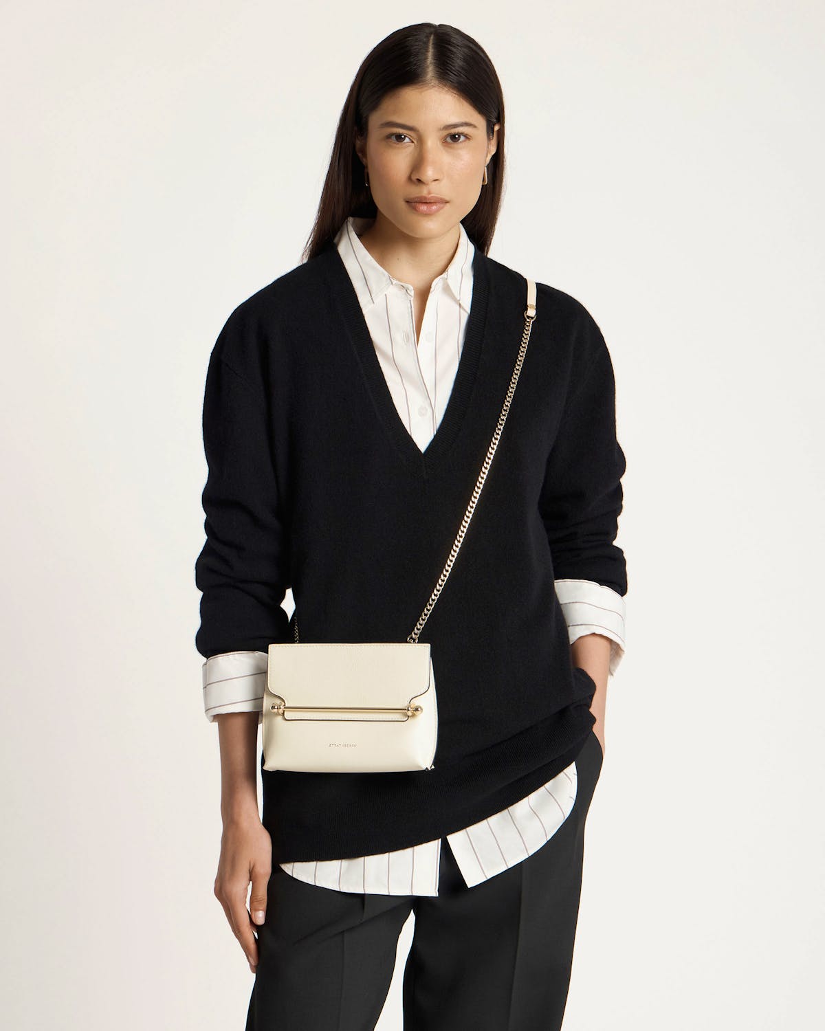 Model wearing black jumper carrying a vanilla leather crossbody bag with gold chain strap