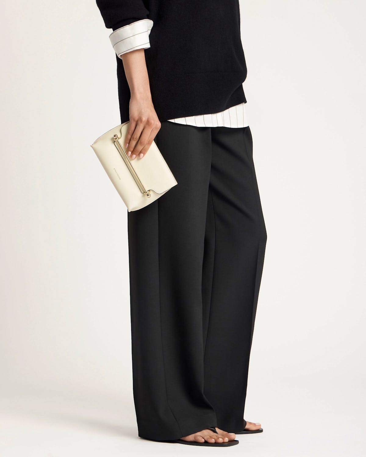 Model holding vanilla Stylist Mini clutch with gold bar handle and Strathberry logo.