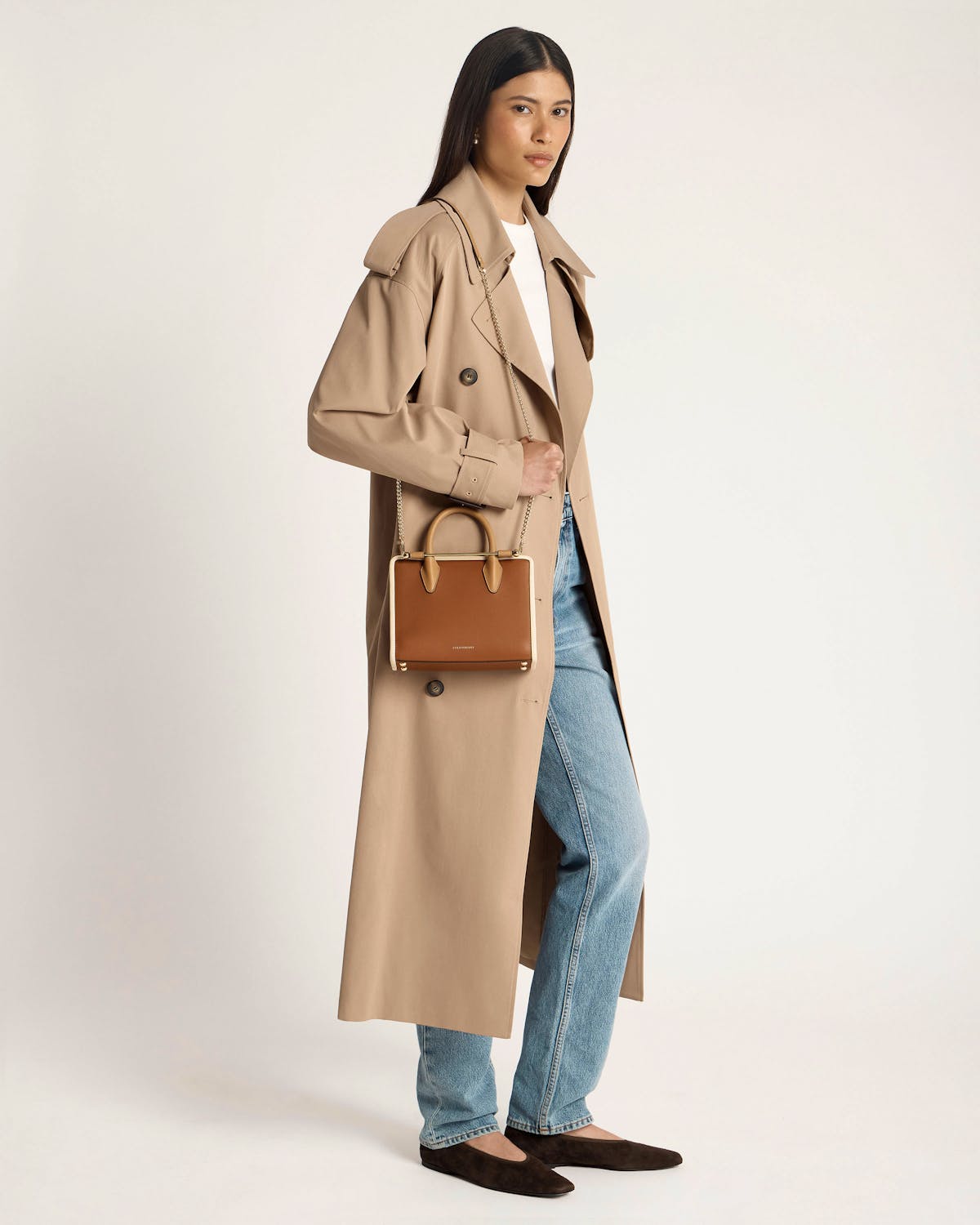 Model in beige trench and jeans carrying a caramel mini tote with cream trim.