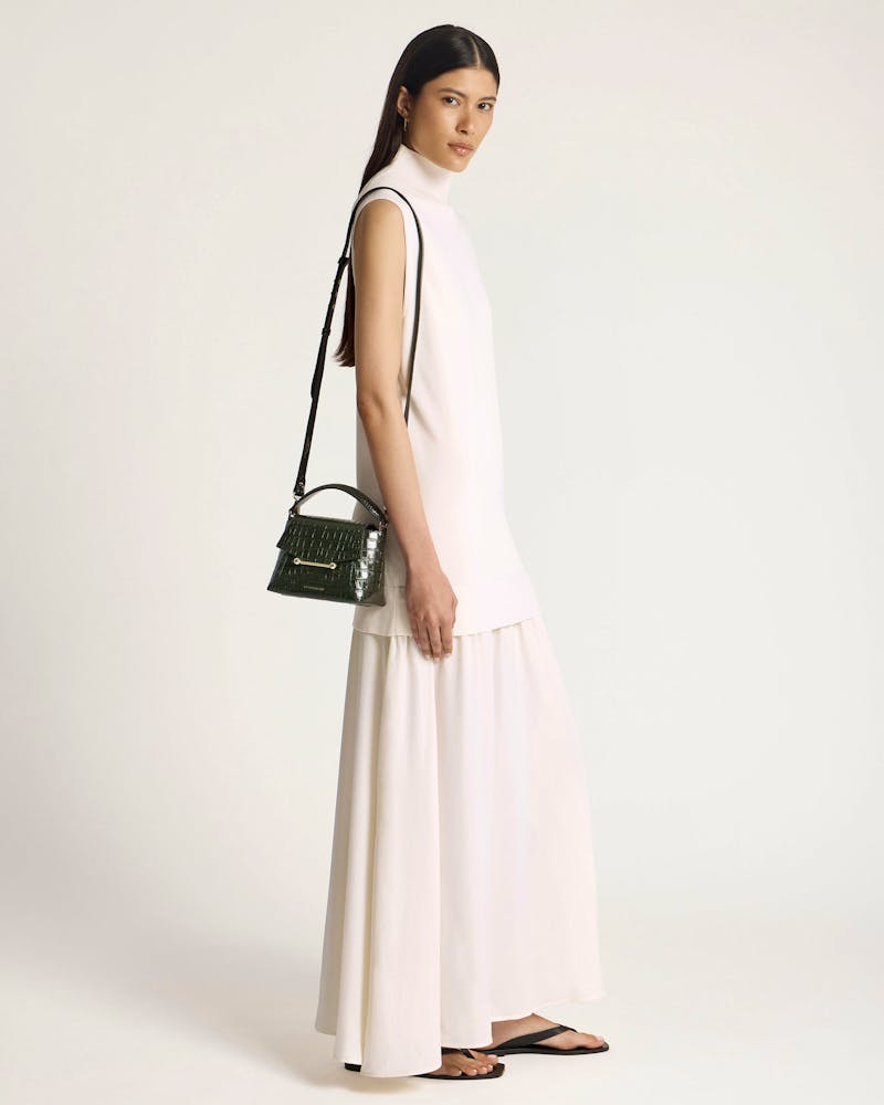 Model in a white sleeveless dress carrying a dark green croc-embossed shoulder bag