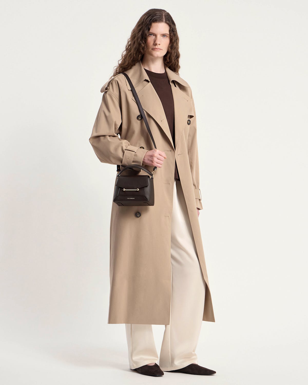 Model wearing a beige trench coat holding an espresso Mosaic Nano bag with shoulder strap.