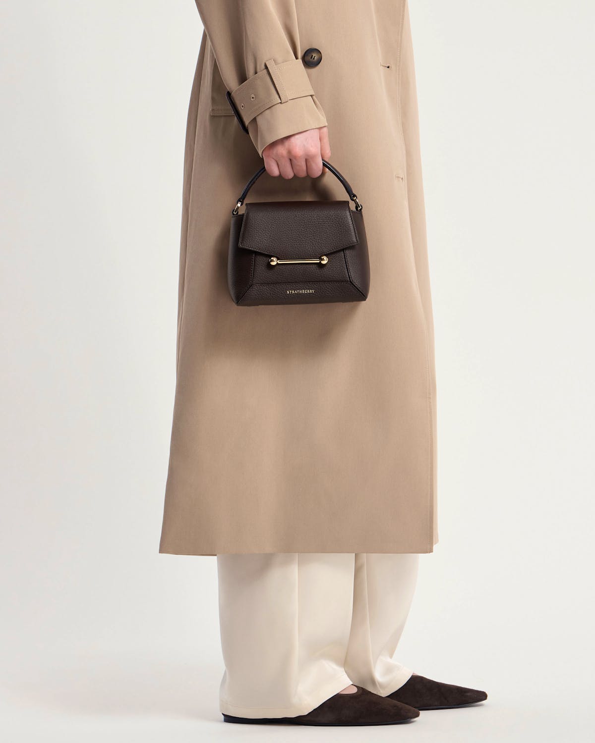 Model holding Strathberry Mosaic Nano bag in espresso with top handle and gold bar
