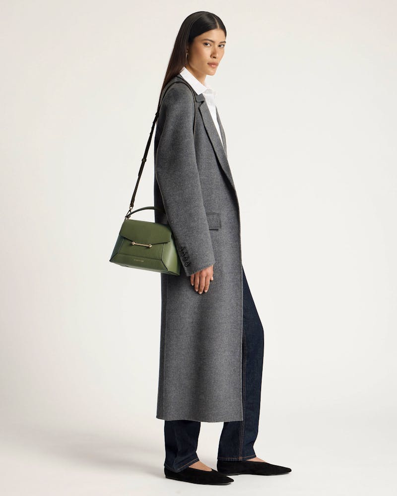 Woman wearing grey coat carrying a pine green mosaic bag over shoulder.