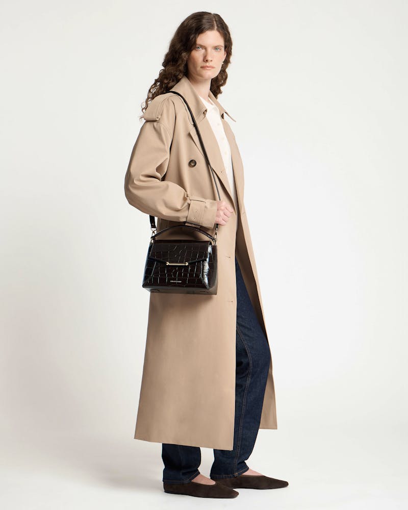 Model wearing a dark croc-embossed mosaic bag over shoulder with beige trench coat.