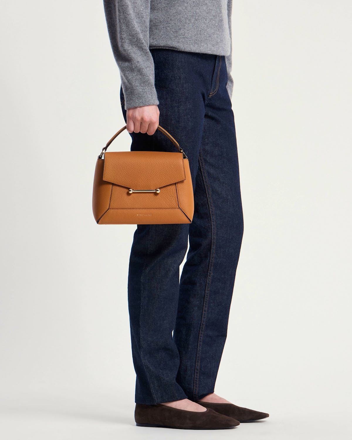 Model holds honey-coloured mosaic bag by top handle beside dark jeans.