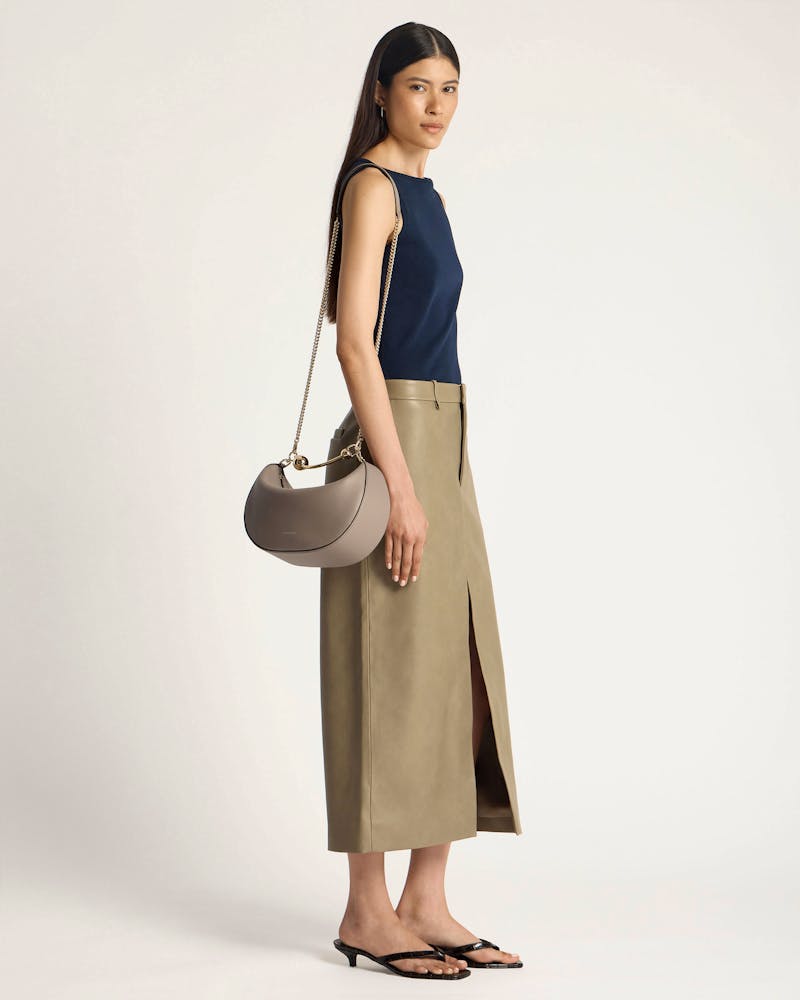 Model wearing a taupe crescent moon shoulder bag with gold chain strap