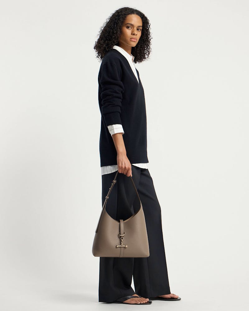 Model holding a taupe hobo shoulder bag with gold hardware and pebbled leather.
