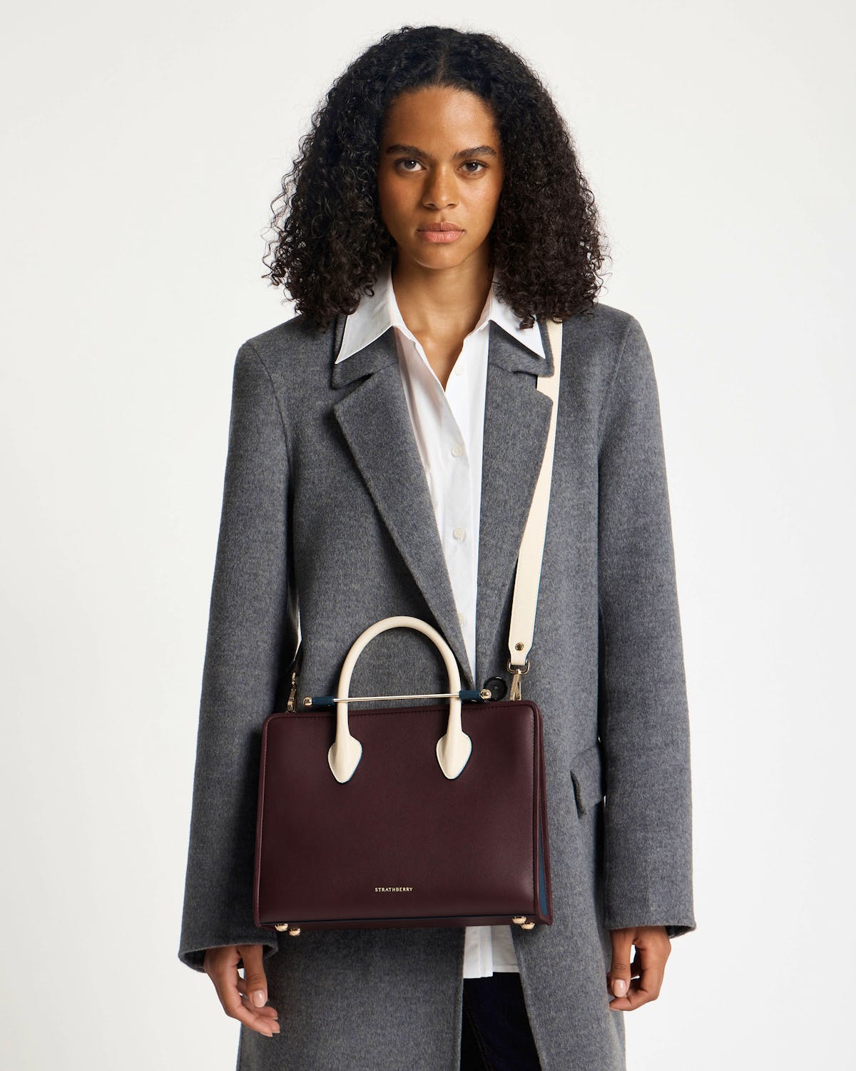 Model carrying a Strathberry midi tote in burgundy, navy and vanilla.
