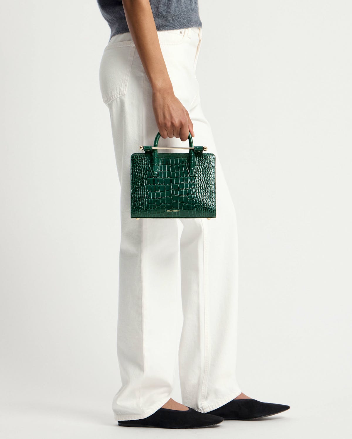 Model's waist down, holding a green croc mini tote bag by Strathberry.