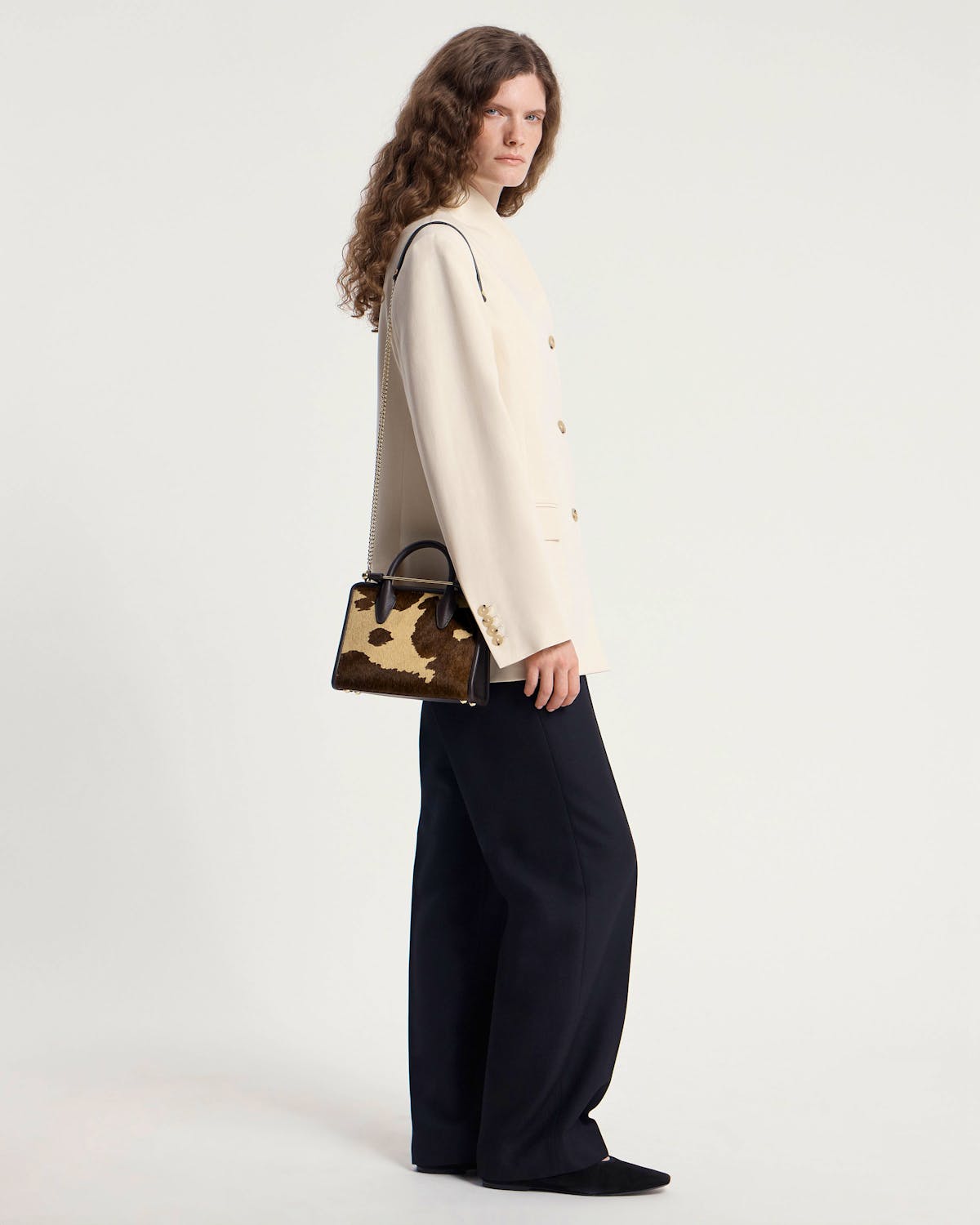 Model wearing cream blazer and trousers holding a sand and espresso spot print mini tote.