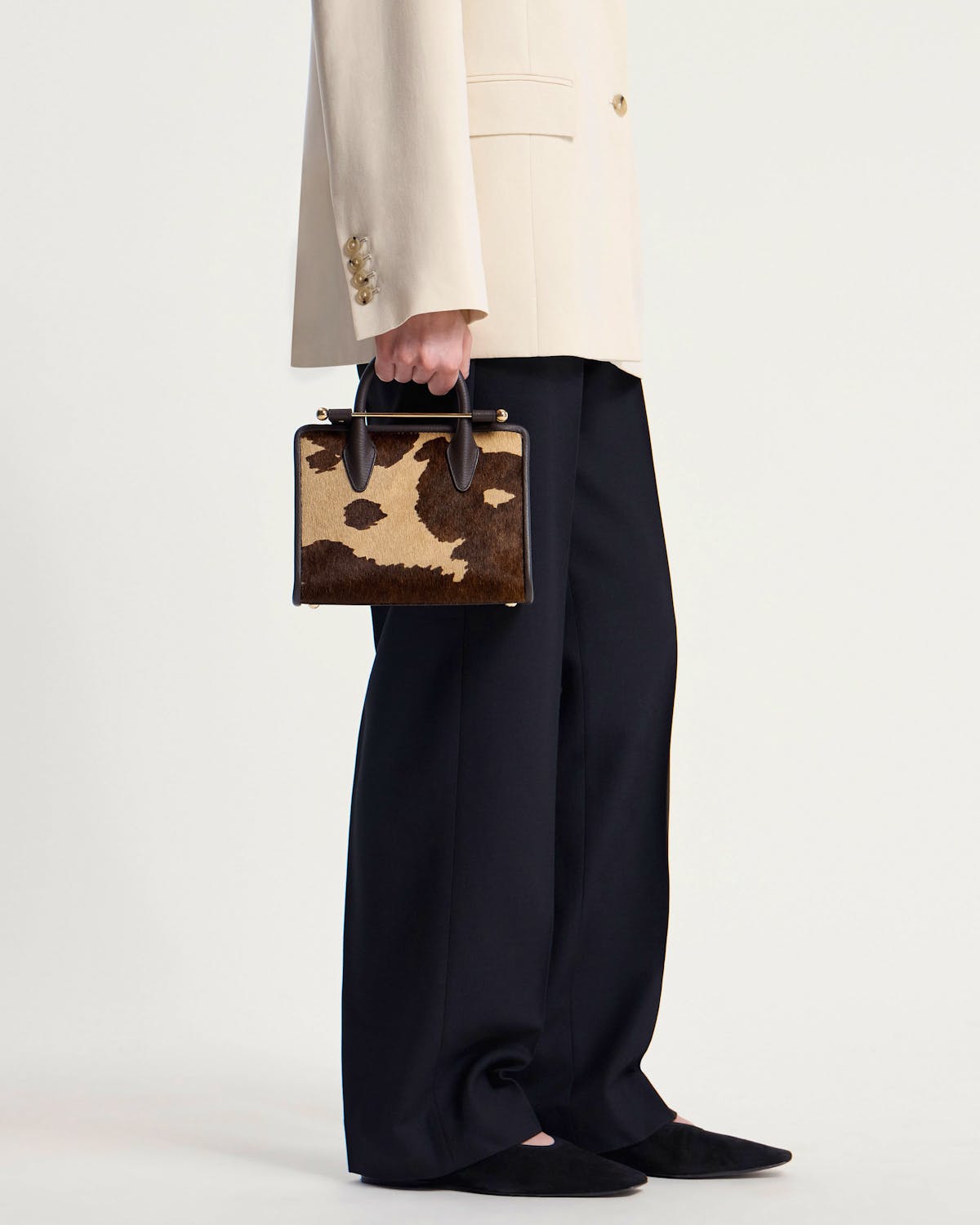 Model holding mini tote with sand and espresso spot print, gold bar handle.