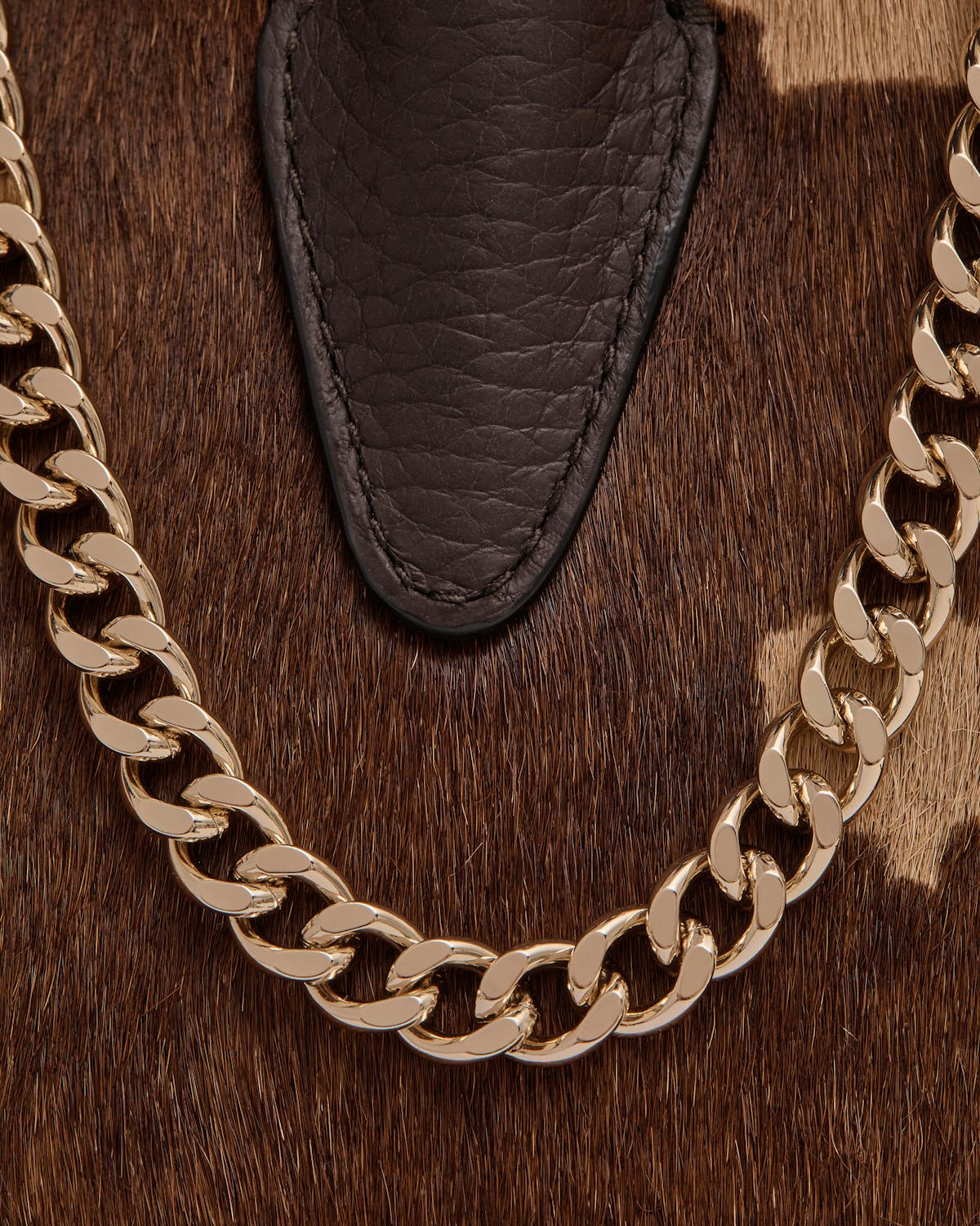 Sand and espresso spot-print hair with dark leather tab and gold chain.