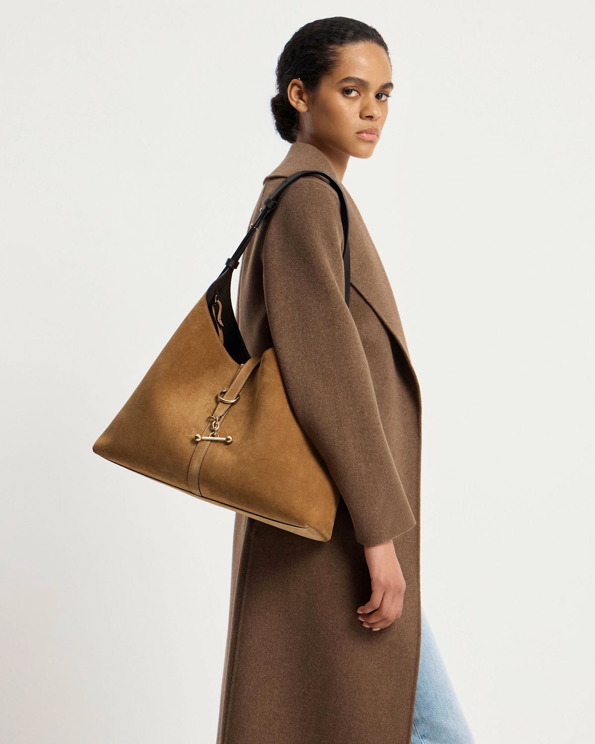 Model carrying toffee suede hobo bag with espresso strap and gold hardware, brown coat.