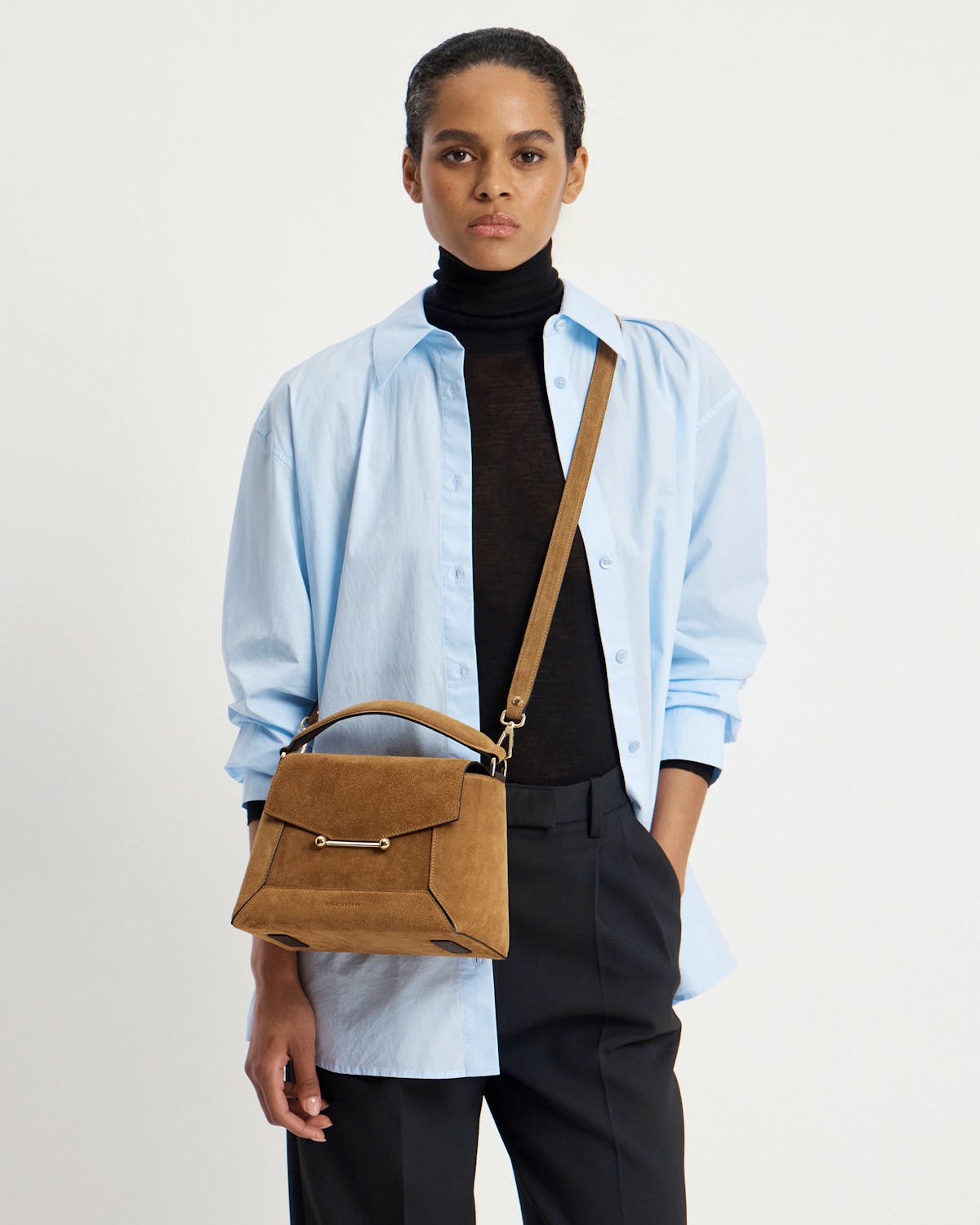 Model in light blue shirt and black roll-neck carrying toffee suede Mosaic bag, espresso strap.