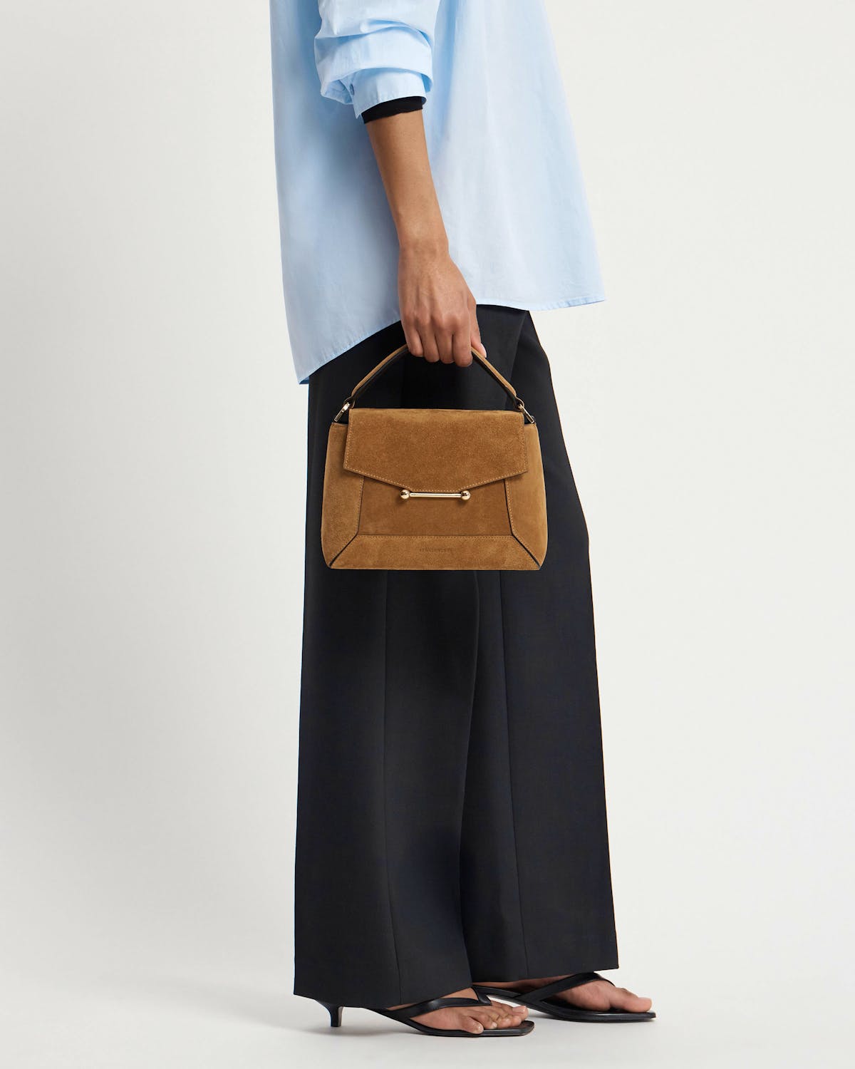 Model holding toffee suede mosaic bag with top handle and gold bar detail.