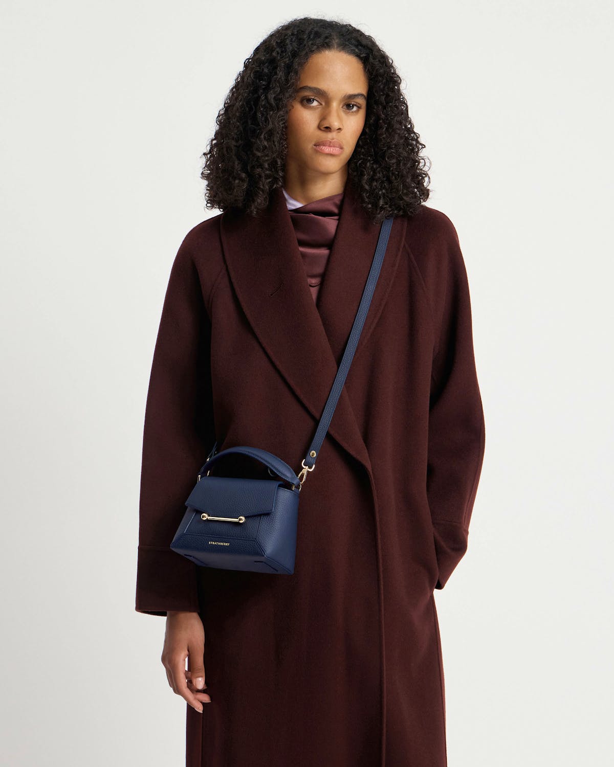 Model wearing navy Strathberry Mosaic Nano crossbody bag over a dark coat