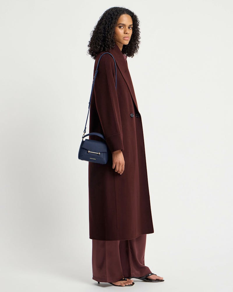 Woman in burgundy coat carrying navy Strathberry Mosaic Nano shoulder bag.