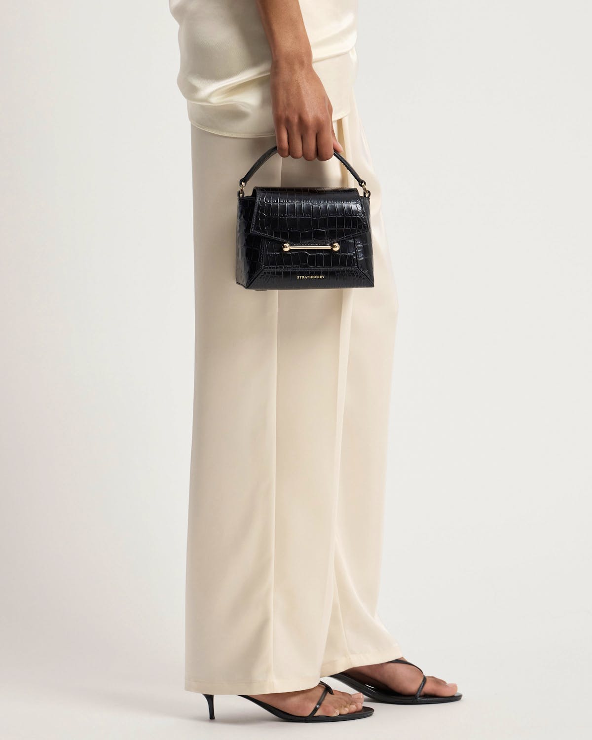 Hand holding Strathberry Mosaic Nano bag in soft croc with gold hardware.