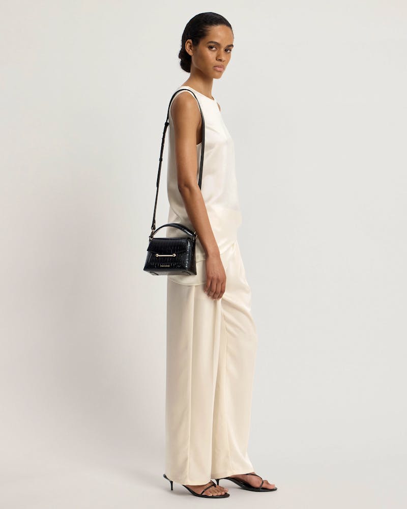 Model in sleeveless white top and cream trousers carrying small black croc bag
