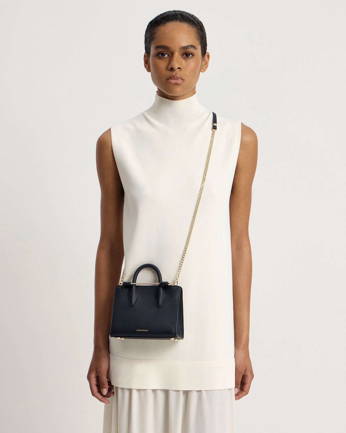 Model wearing white sleeveless dress with black Strathberry Nano Tote crossbody bag.