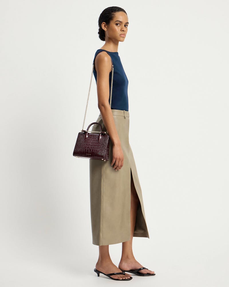 Model wearing a navy top and beige skirt carrying a burgundy croc mini tote.
