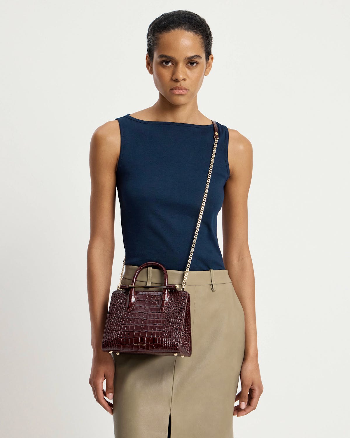 Model wearing navy sleeveless top and beige skirt with Strathberry burgundy croc mini tote.