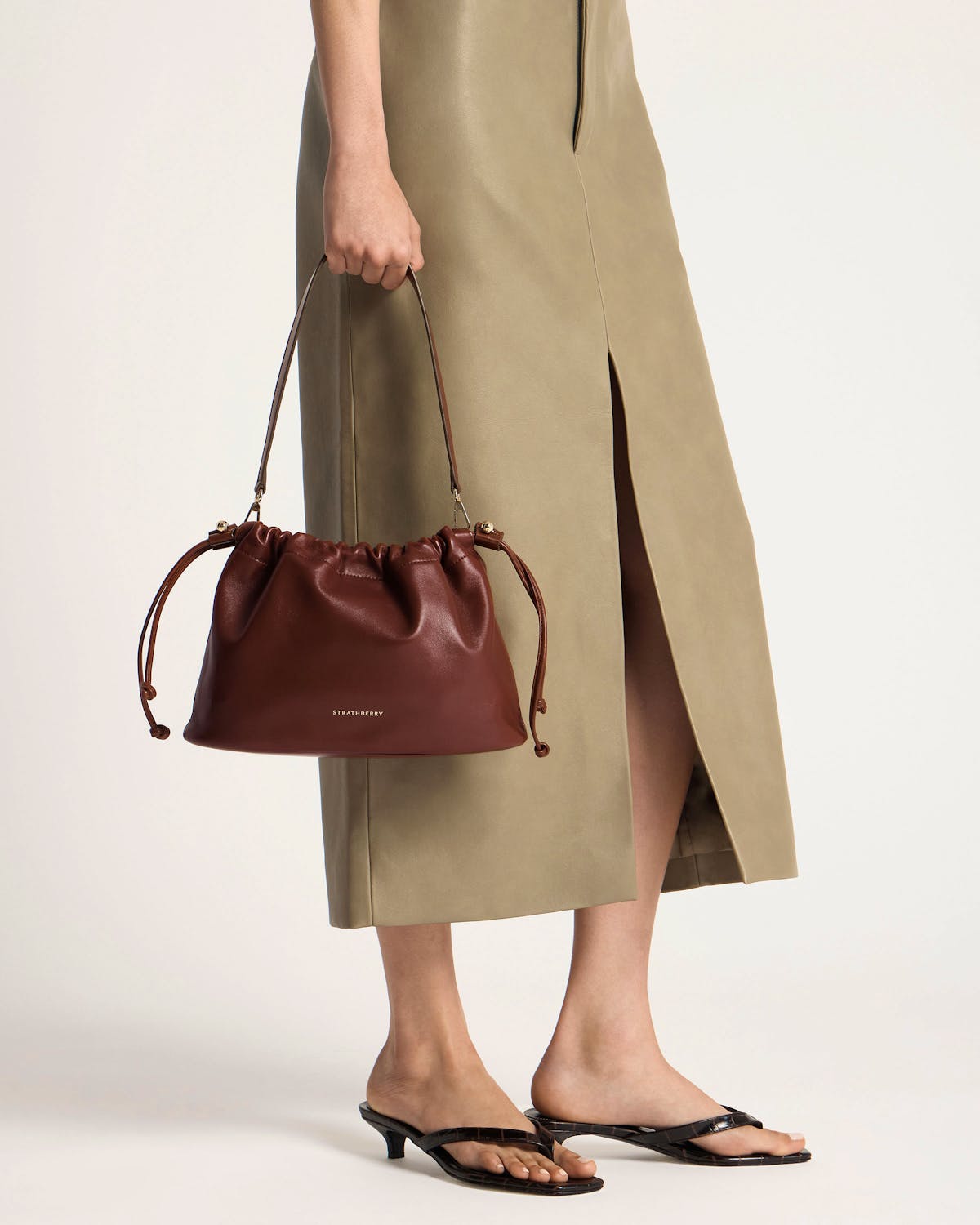 Strathberry walnut Charlotte midi drawstring bag held by model at her side.