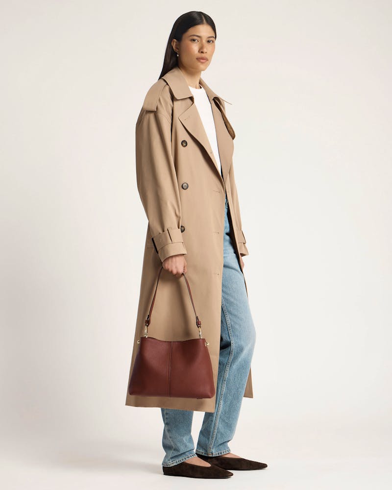 Woman in trench coat holding a walnut Lana hobo leather bag by the handle.