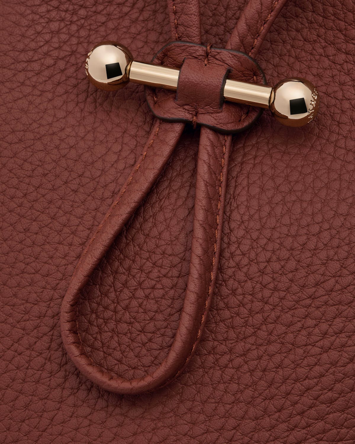 Pebbled walnut leather surface with drawstring cords and gold bar toggle fastener.