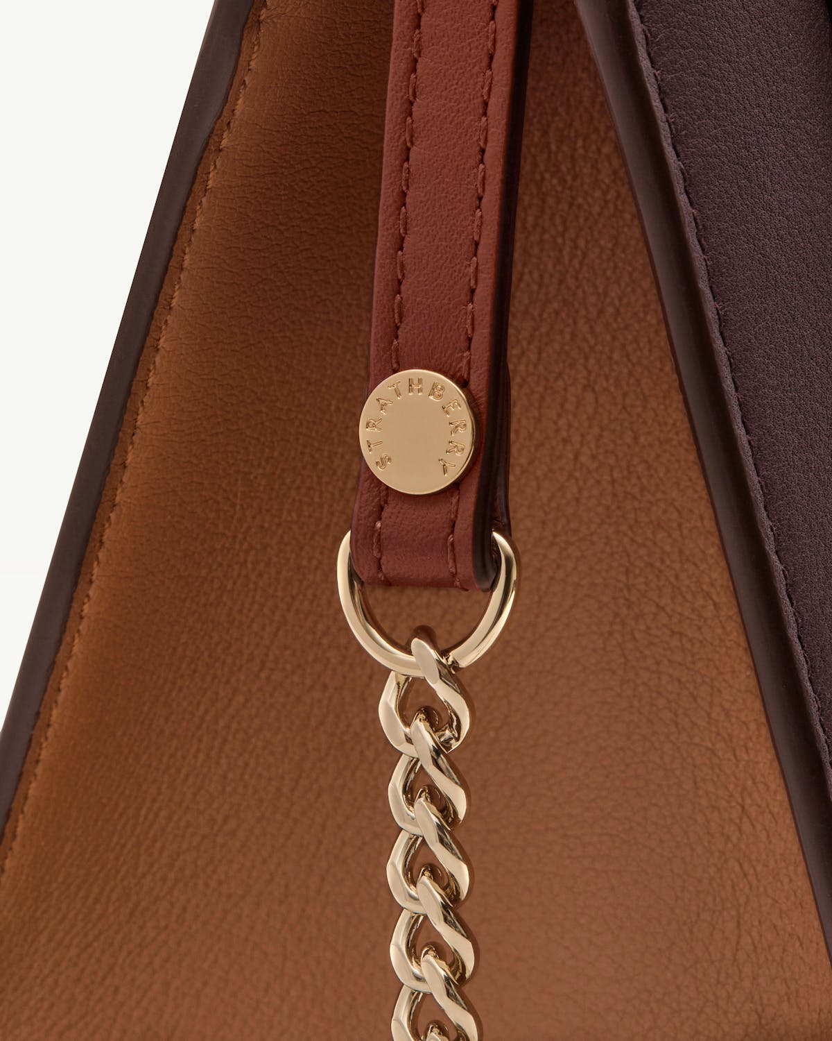 Burgundy leather strap with gold Strathberry disc and chain on chestnut and walnut leather.