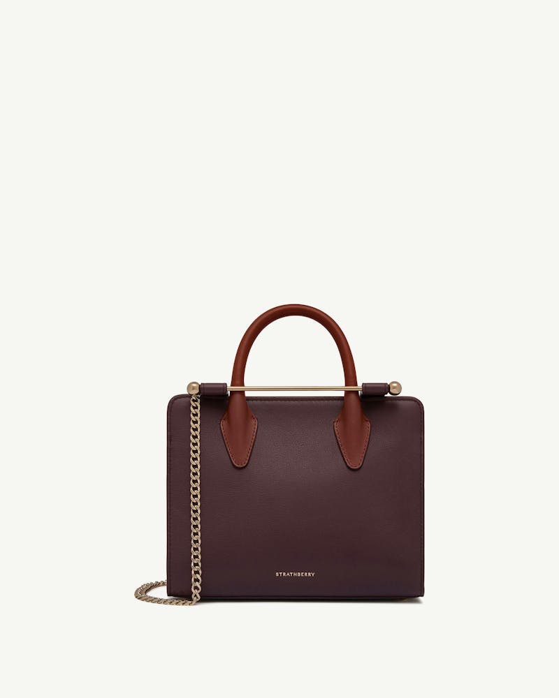 Burgundy mini tote with chestnut handles, gold chain strap and Strathberry logo.