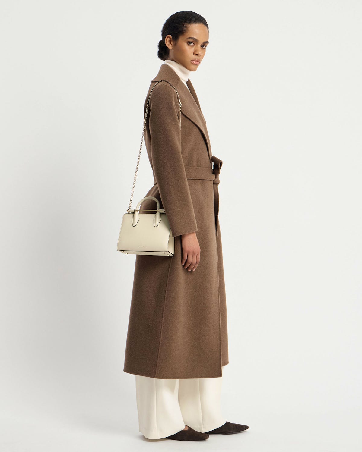 Model wearing a brown coat carrying a vanilla mini tote bag with chain strap.