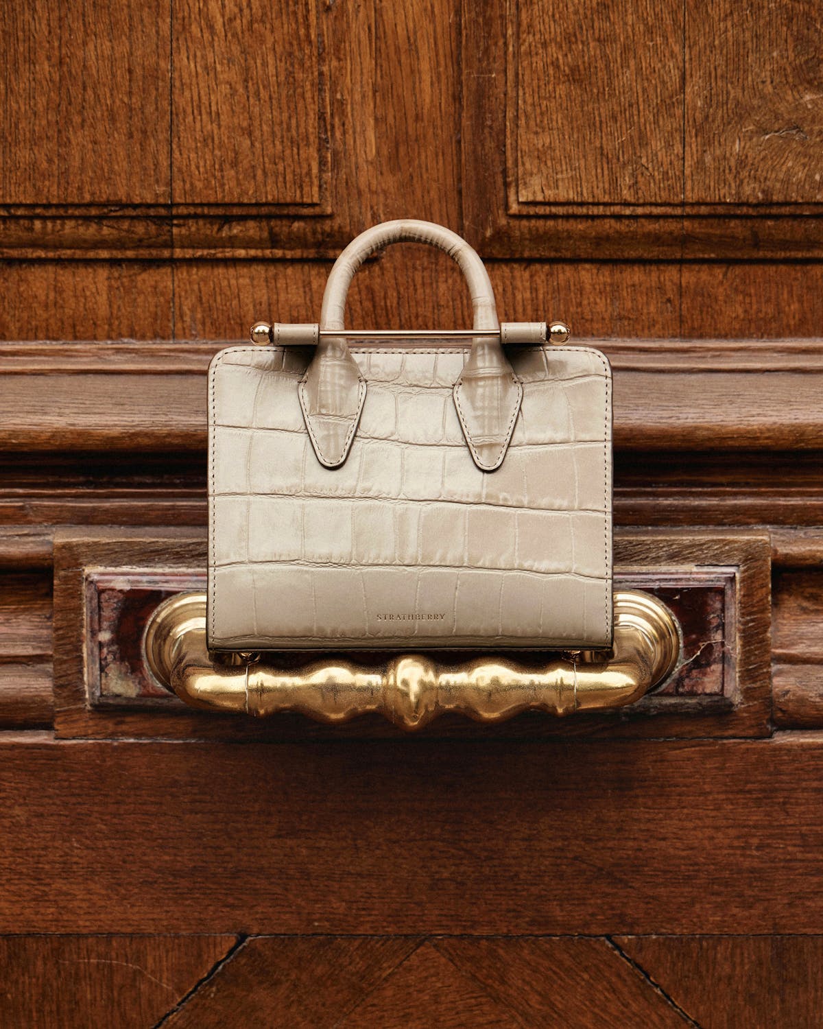 Strathberry nano tote in croc leather on a wooden door handle.