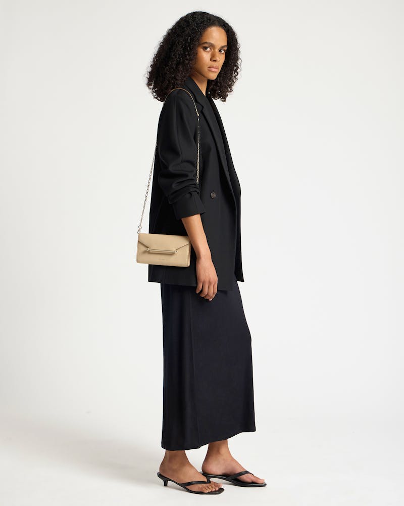 Model wearing sand leather chain wallet with gold chain strap over black blazer.
