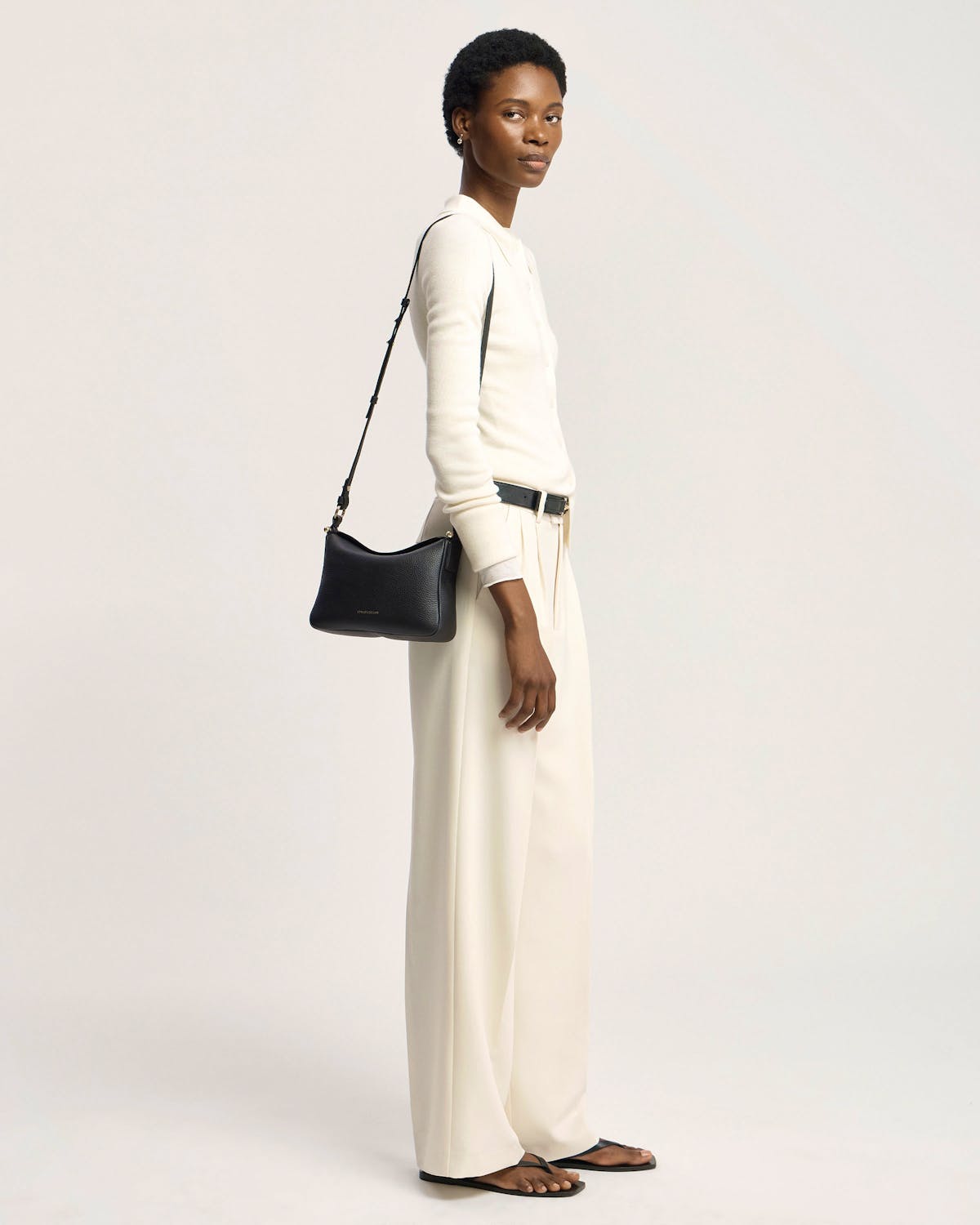 Model in white outfit carrying black Strathberry Sway shoulder bag